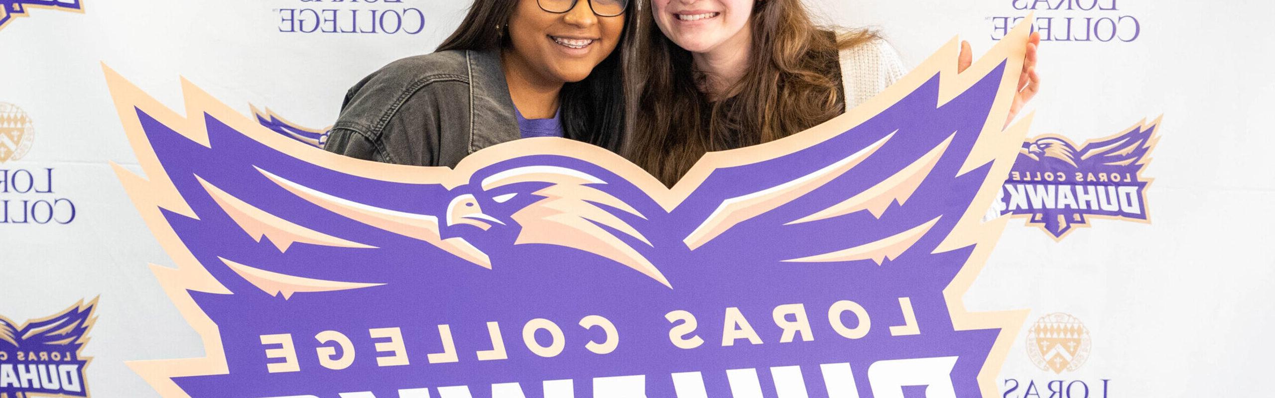 two students smiling with duhawk pride while holding up banner with the Duhawk Athletics Logo